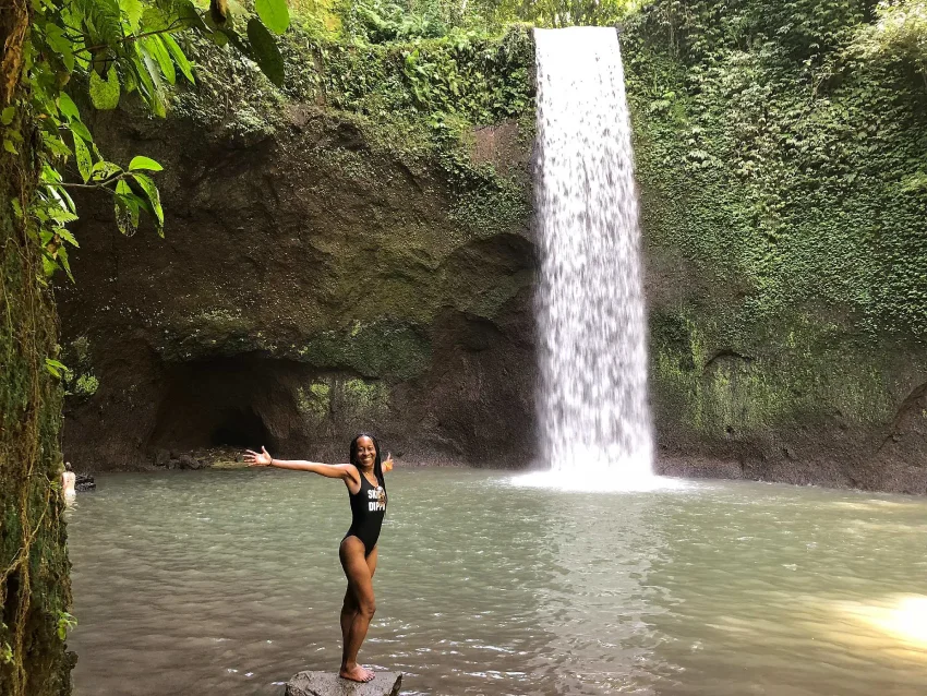 Woman posing with arms wide open at a lush tropical waterfall